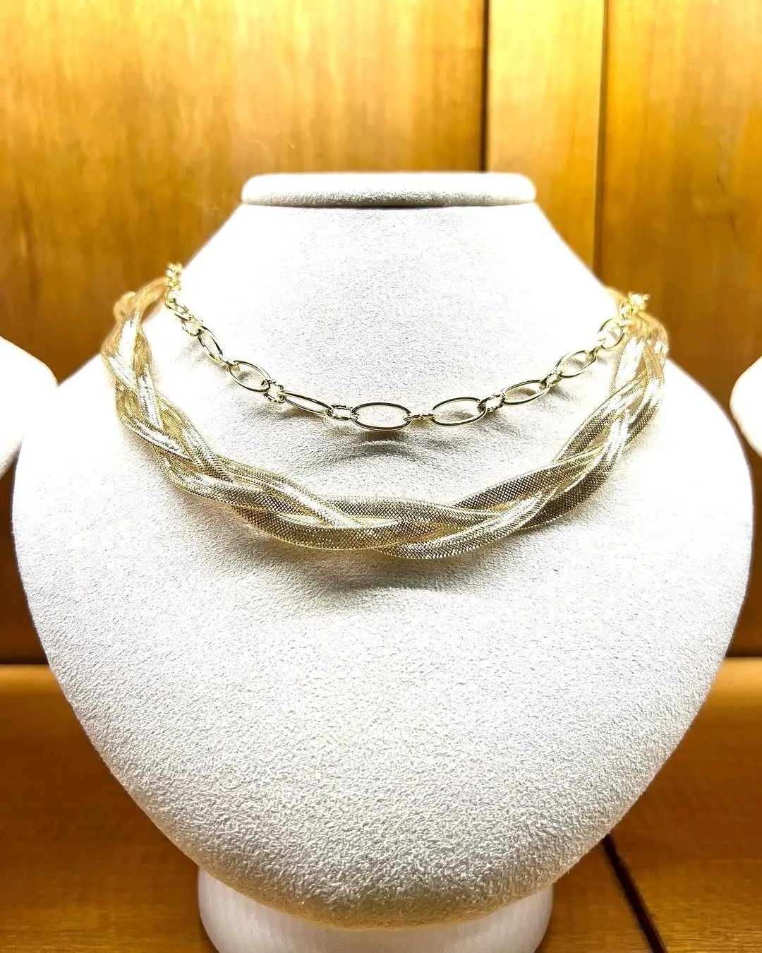 Una catena intrecciata e una a maglie ovali, in oro giallo e bianco, su un busto chiaro
