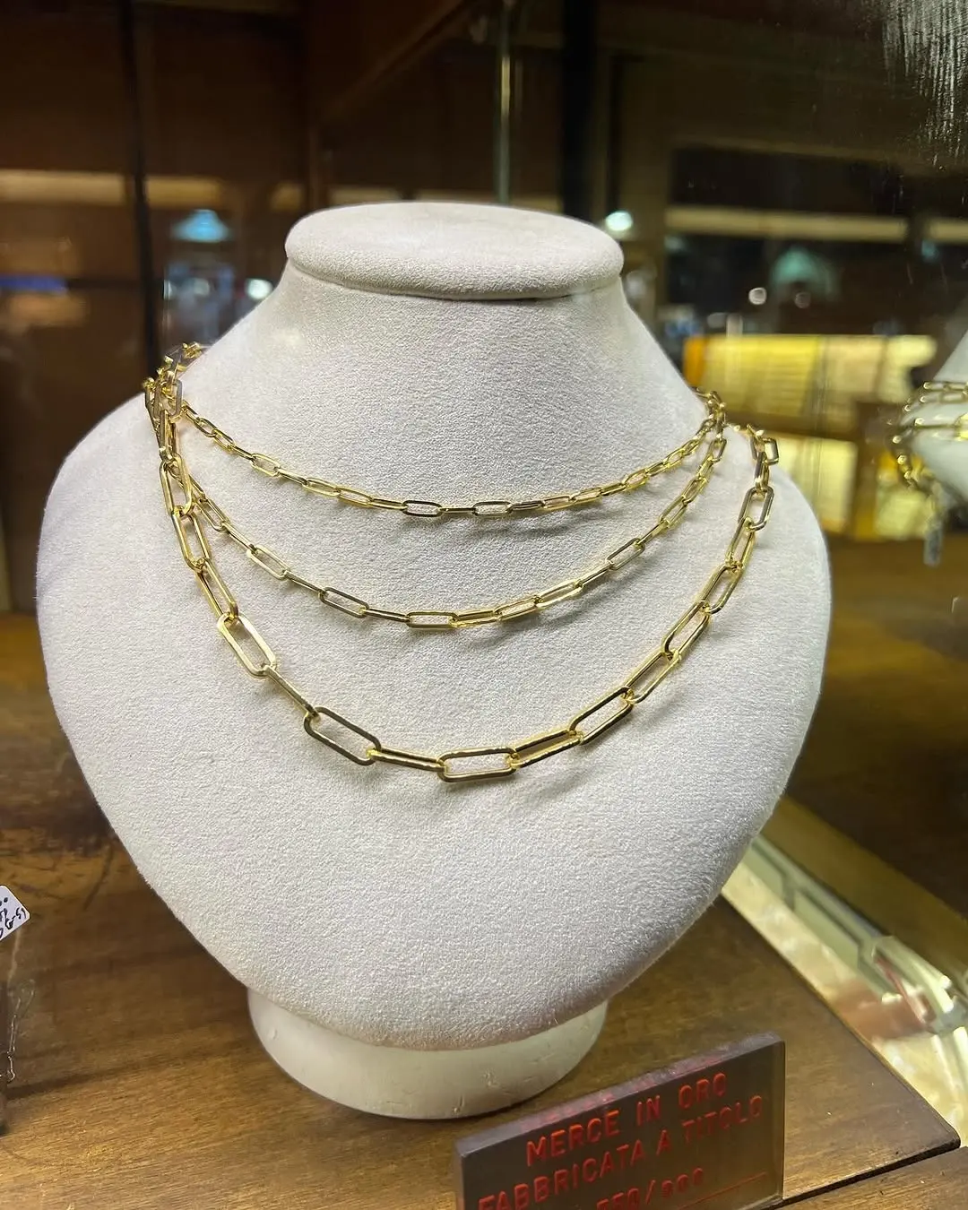 Tre catene d'oro a maglia lunga una sopra l'altra, su un busto chiaro in vetrina