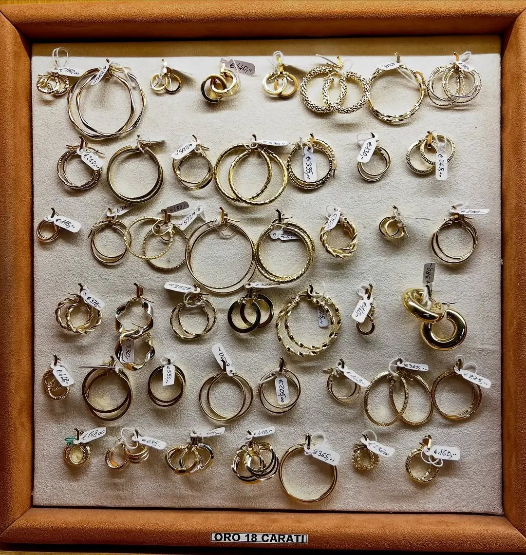 Il vassoio della vetrina pieno di orecchini a cerchio in oro, ognuno col suo cartellino bianco