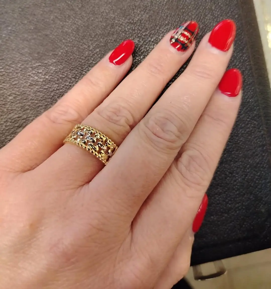 Una fascia traforata in oro bianco e giallo all'anulare di una mano con lo smalto rosso