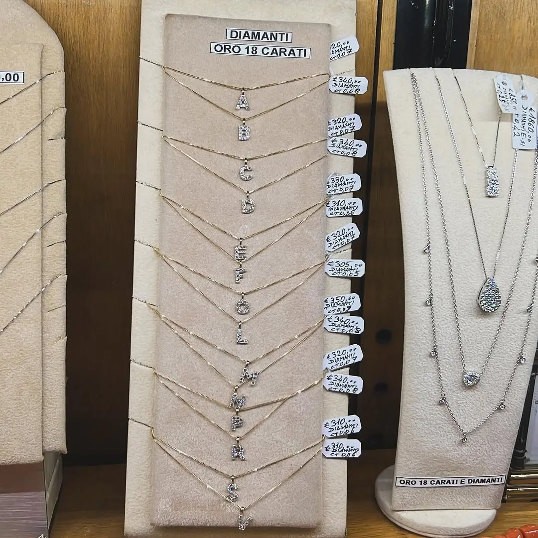 Le catenine con le lettere dell'alfabeto in oro 18 carati e diamanti, appese in fila in vetrina con i loro cartellini