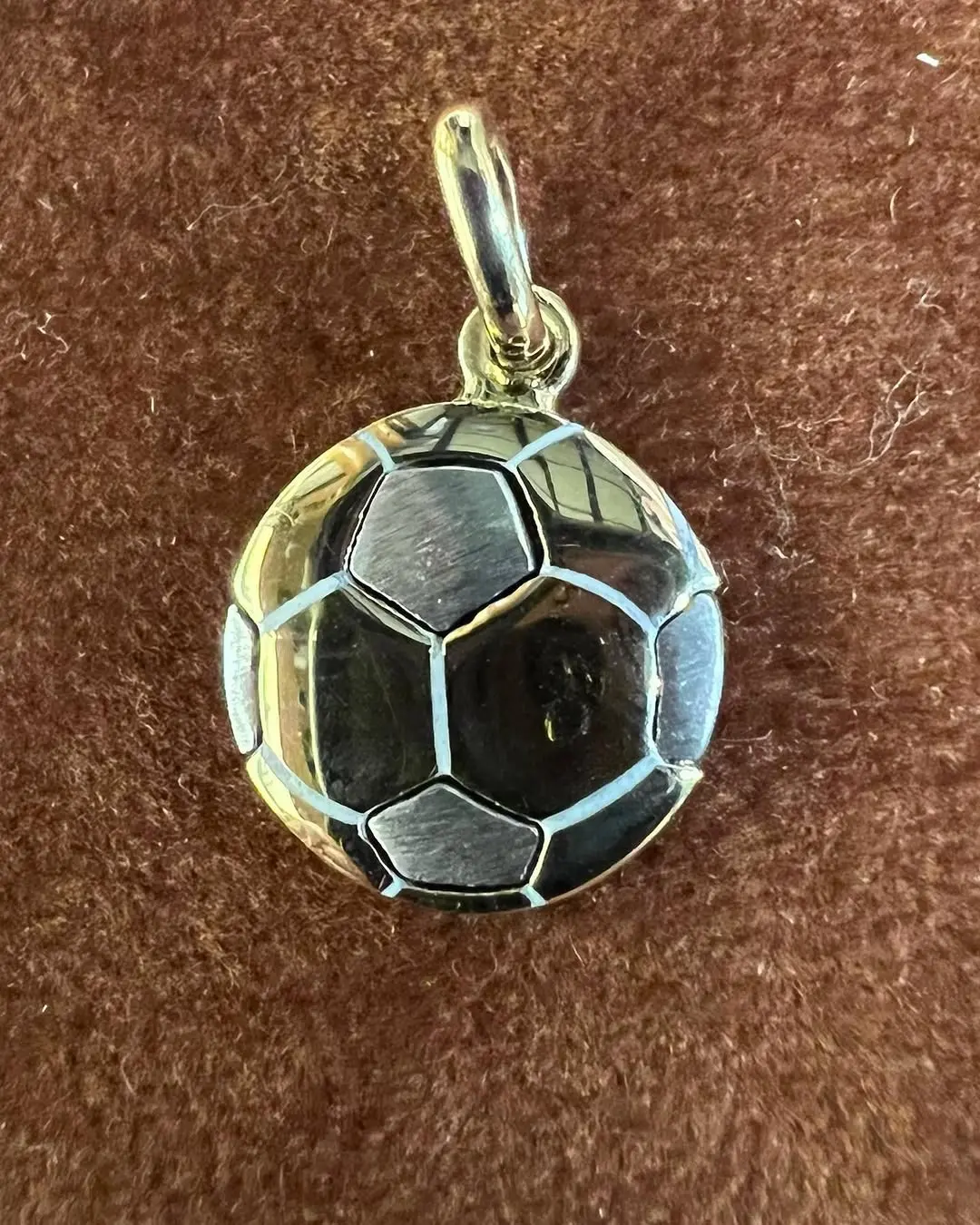 Il ciondolo a forma di pallone in oro giallo e bianco, sul velluto marrone